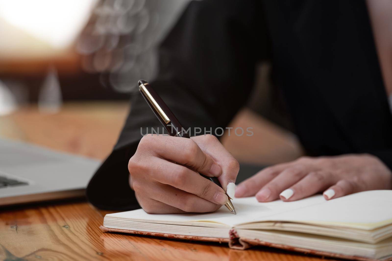 Close up hand of woman hand holding pen taking note and working with laptop at the table office by nateemee