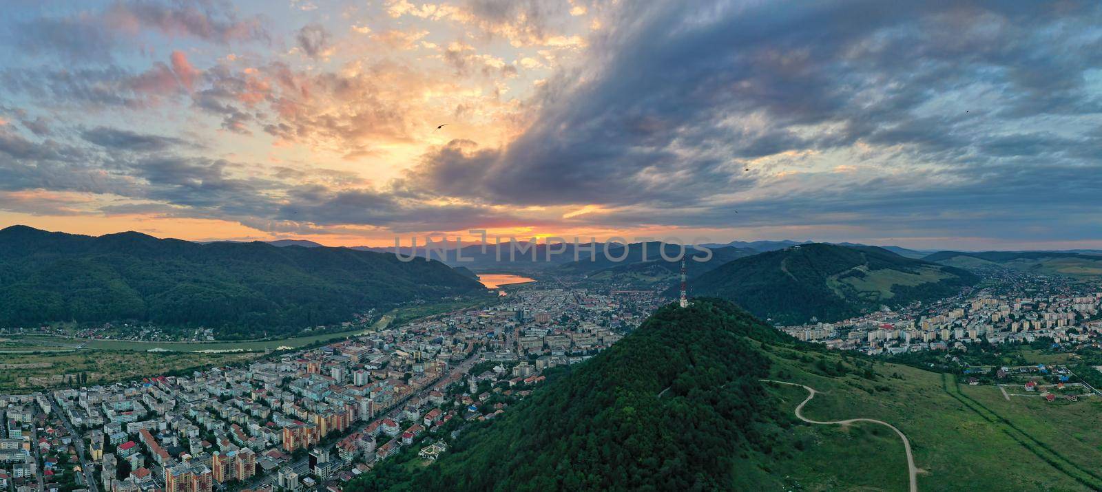 Sunset panorama over green mountain city in Romanian Carpathians, aerial summer landscape of Piatra Neamt city surrounded by forest.