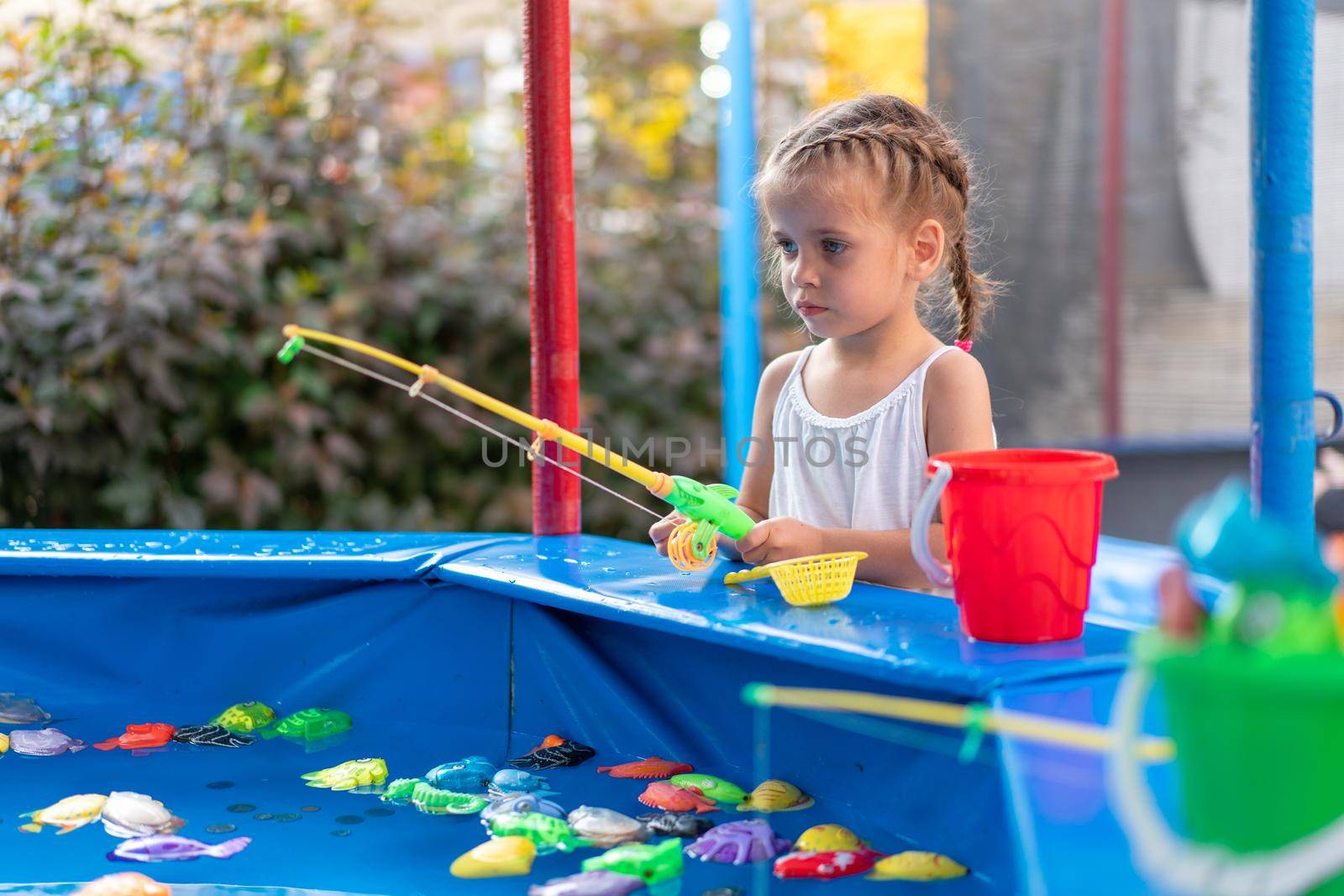 Child Fisher Catching Plastic Toy Fish On Pool Amusement Park Summer Day Little Girl Have Fun On Fishing Carnival Festival Entertainment For Children