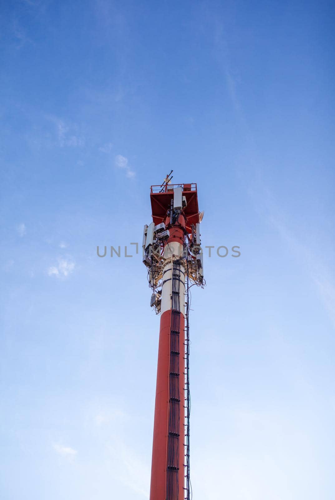 A white and red tower with cellular communication antennas on a sky by AnatoliiFoto