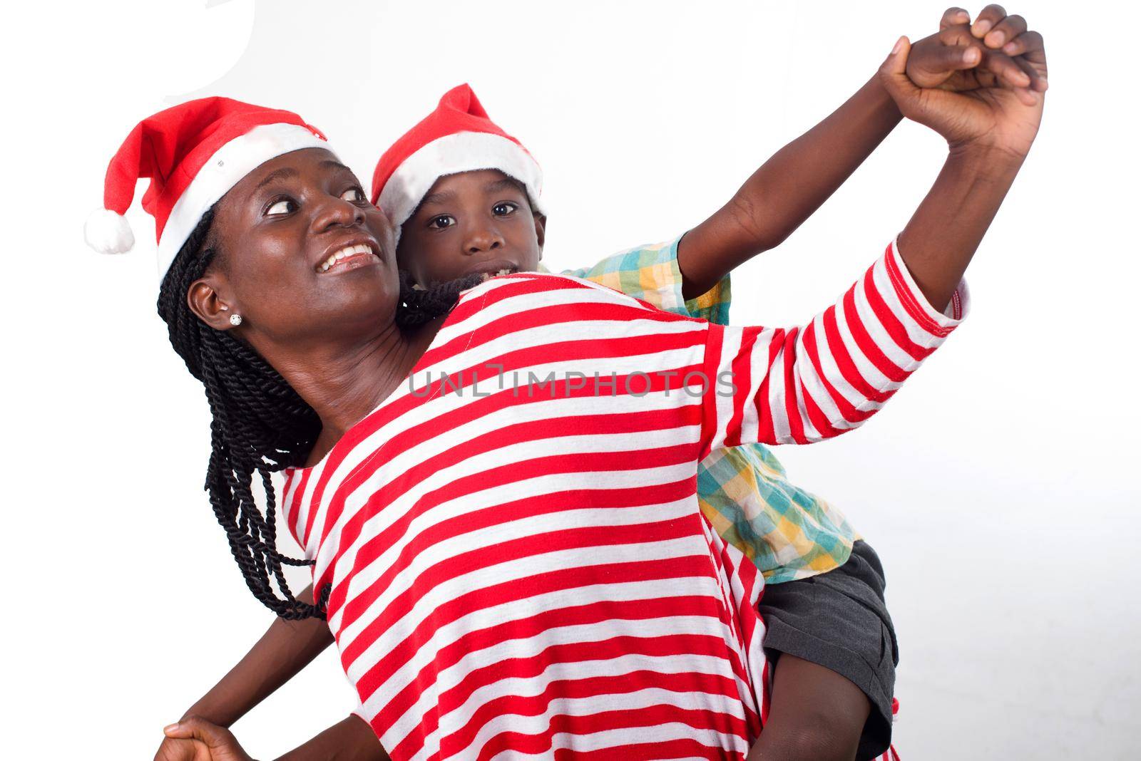 child on the back of his mother with Santa's hats both look in the same direction with outstretched arms.