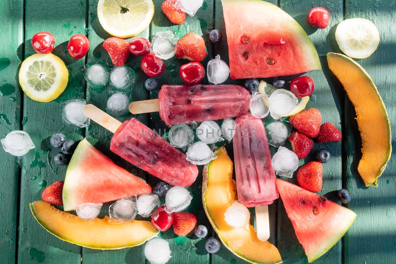 Photographic shot of popsicles made with red fruit on a table served with various fruit 