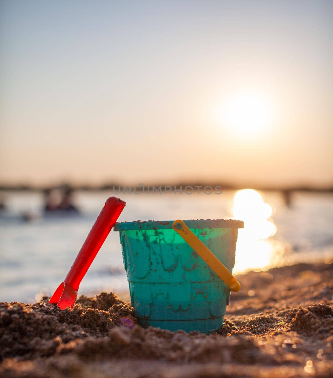 Children's toys for playing on the sand. Plastic bucket and rake on the beach at sunset. The concept of summer, family holidays and vacations.
