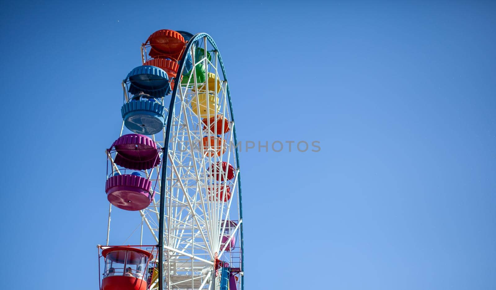 A large Ferris wheel against a blue sky. Booths with people go up. There is a place for the text. Concept: entertainment on summer holidays, holidays with children on weekends, ride on rides.