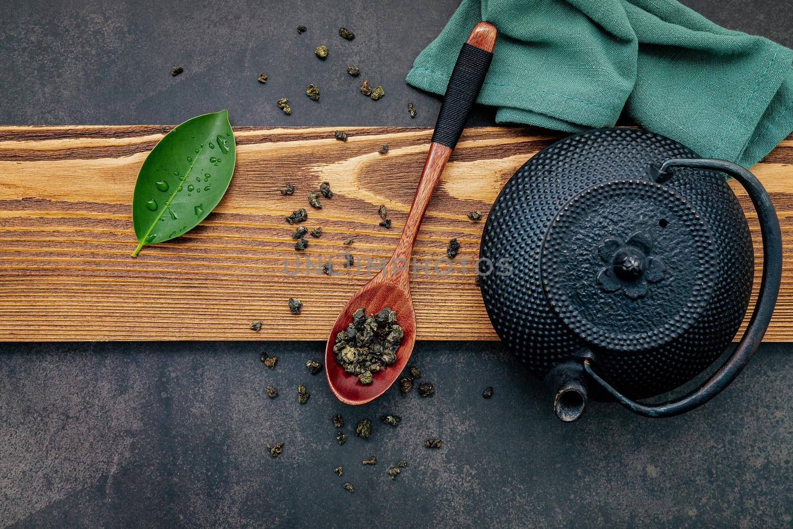 Black cast iron tea pot with herbal tea set up on dark stone background.