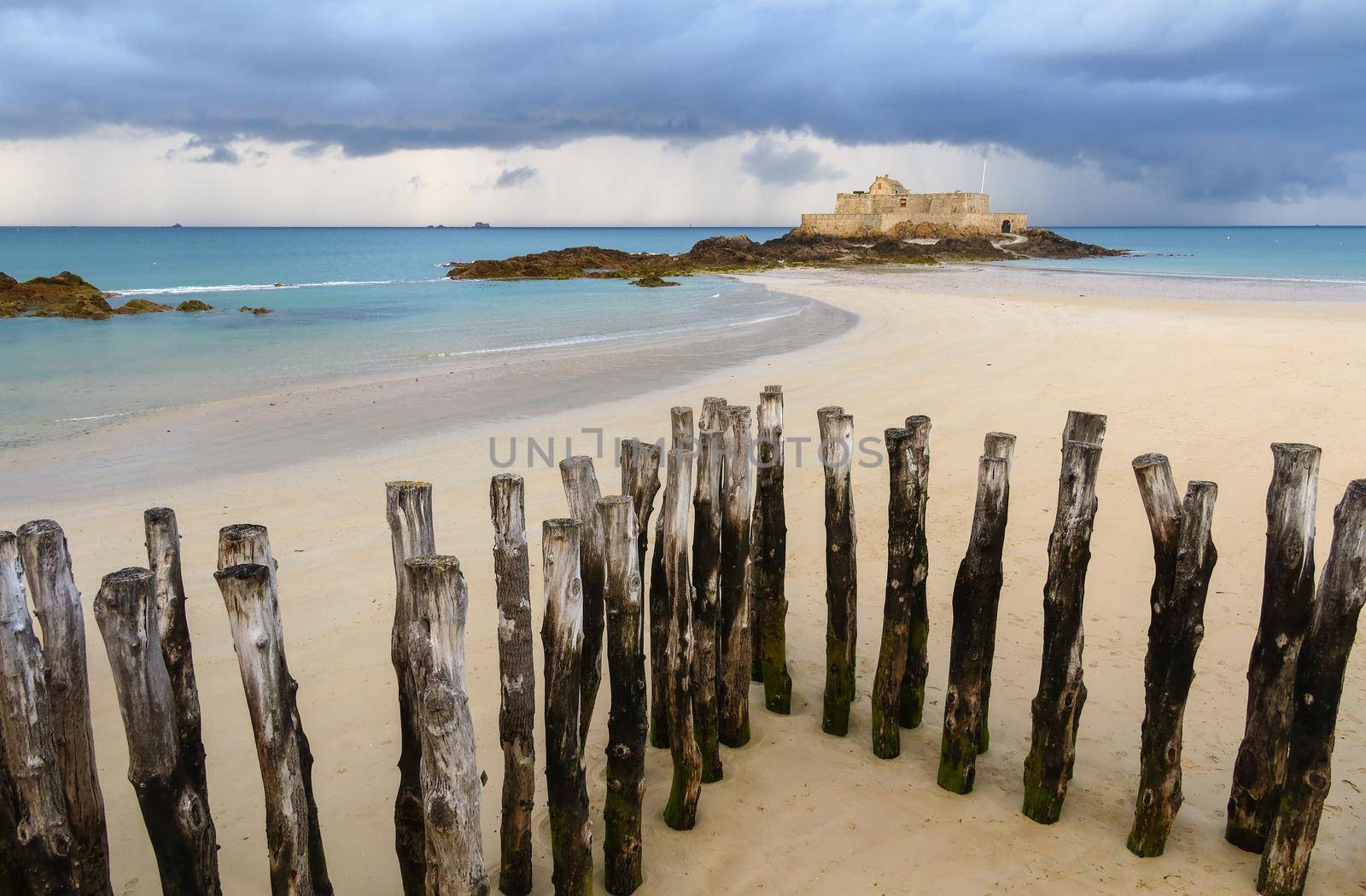 Fort National in Saint-Malo and breakwater trunks at eventail beach during low tide. Brittany, France