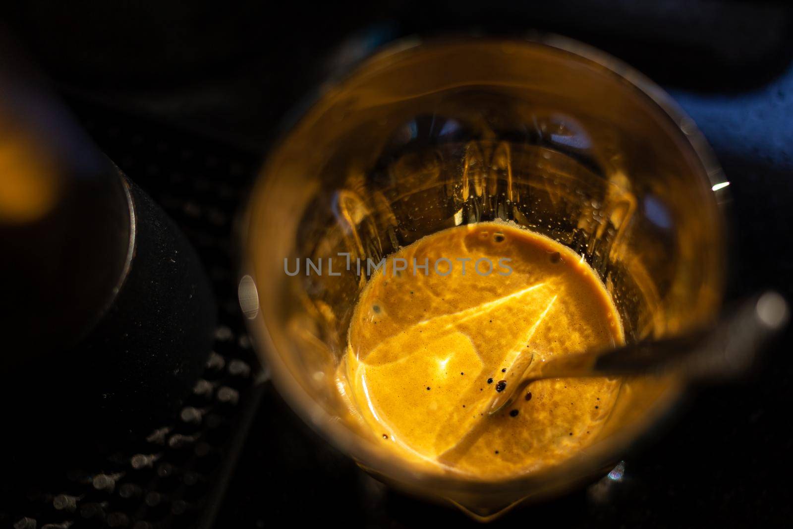 Close focus on crema of hot espresso coffee on glass cup with dark scene of table.