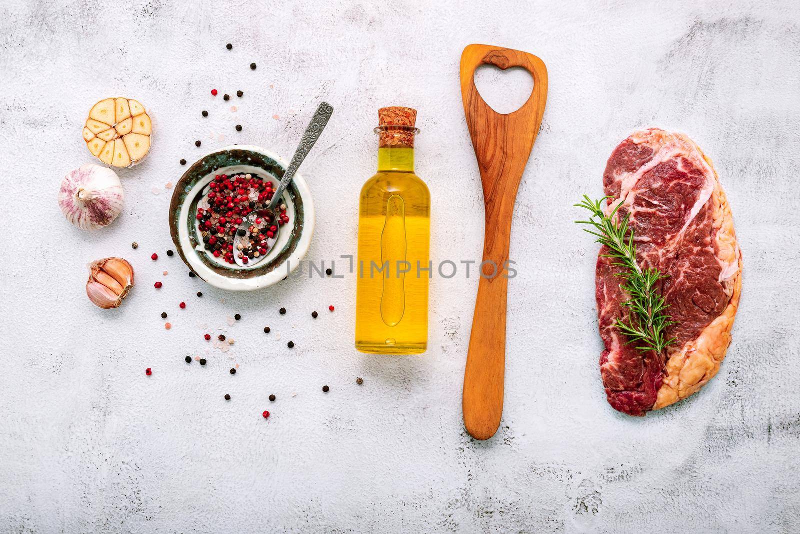 Raw Striplion Steak set up  on white concrete background. Flat Lay of fresh raw beef steak with rosemary and spice on white shabby concrete background top view. by kerdkanno