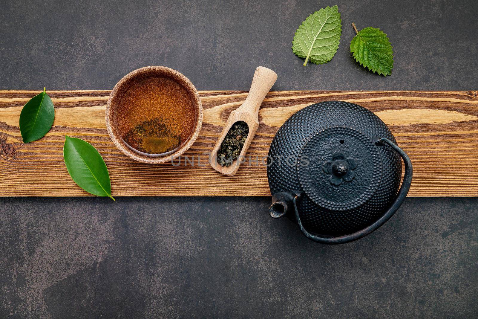 Black cast iron tea pot with herbal tea set up on dark stone background.