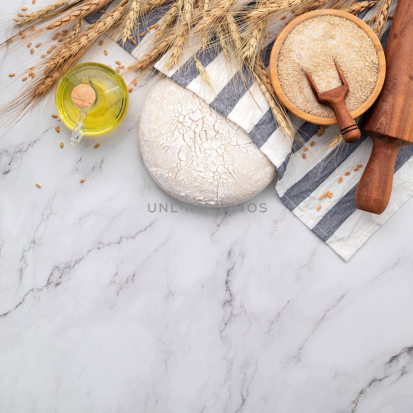 Fresh homemade yeast dough resting on marble table with ears of wheat and rolling pin.