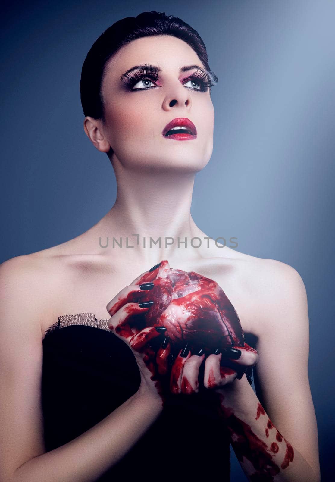 Beautiful young woman holding a bloody human heart against light blue background