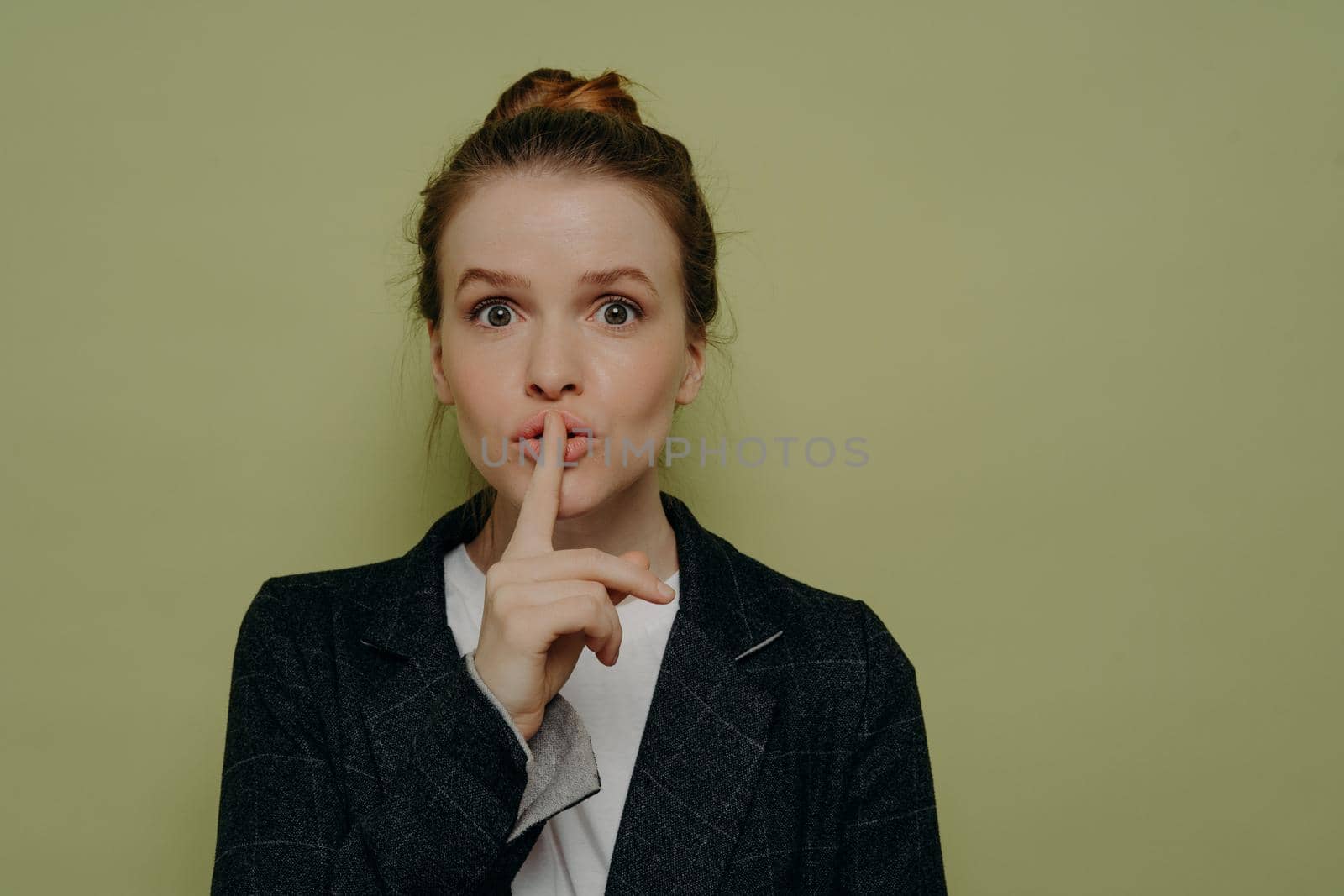 Mysterious young woman in casual wear asking to be quiet or keep something in secret, young female making shushing or silence gesture with finger on lips while standing in studio. Secrecy concept