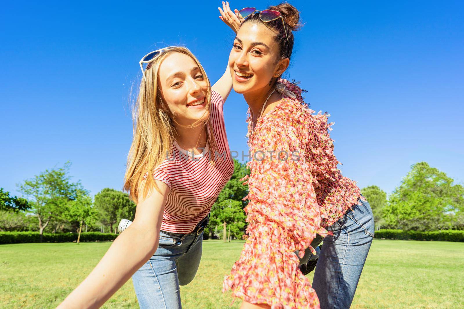 Two women best friends having fun in a city park posing for a happy selfie smiling looking at camera. Two homosexual student girl enjoying diversity joking together outdoor in the green of nature