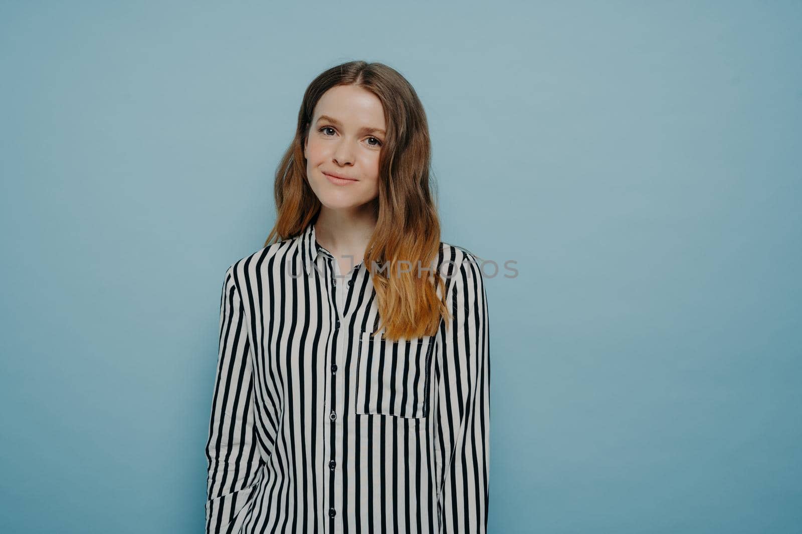 Studio shot of smiling young woman wearing casual clothes feeling relaxed and having happy expression while posing against blue background in studio, happy teenage girl expressing good emotions