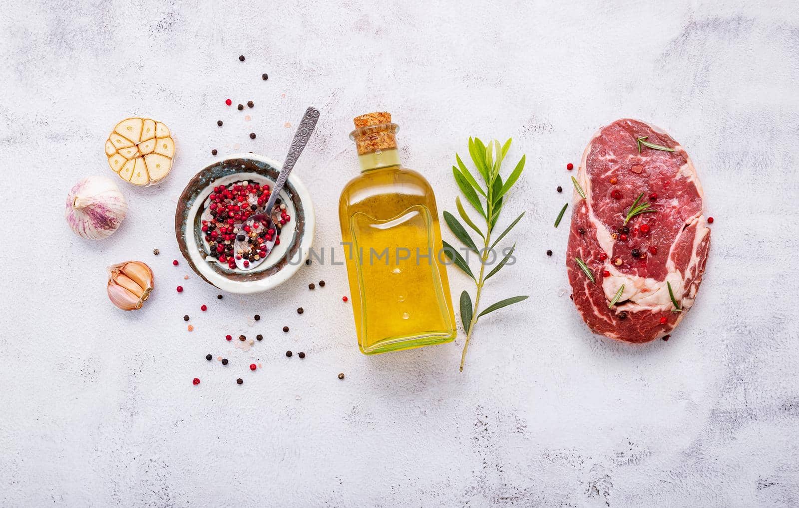 Raw Rib Eye steak set up  on white concrete background. Flat Lay of fresh raw beef steak with rosemary and spice on white shabby concrete background top view. by kerdkanno