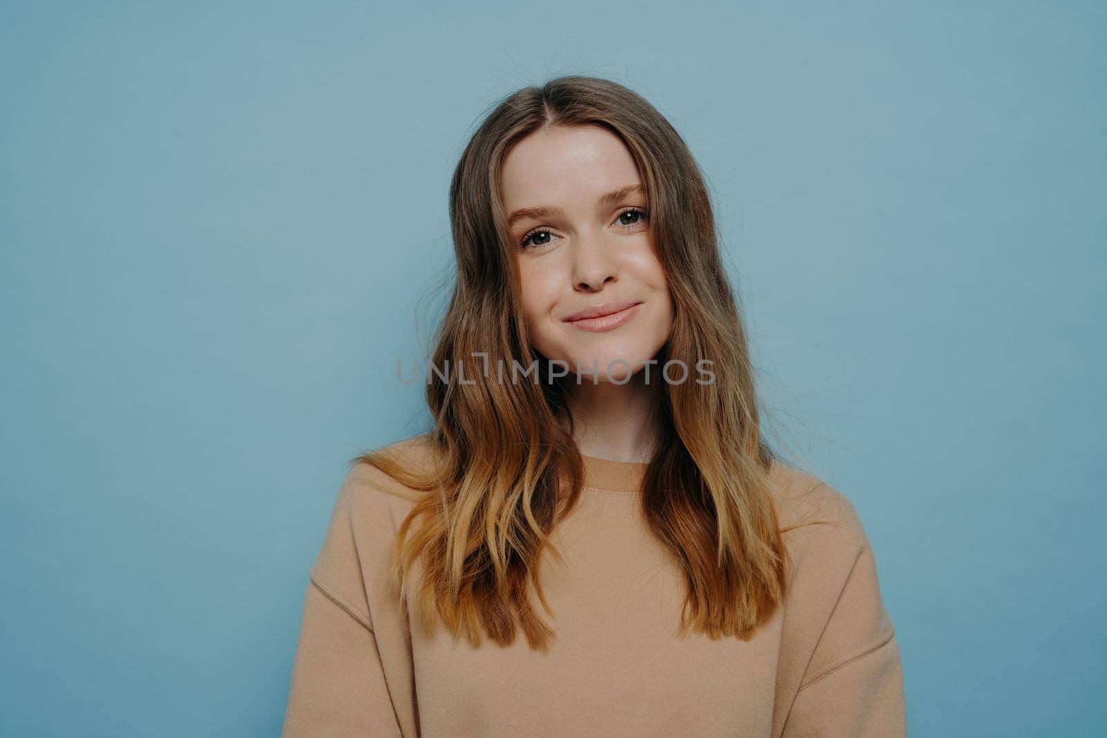 Positive young girl smiling at camera posing over blue background by vkstock