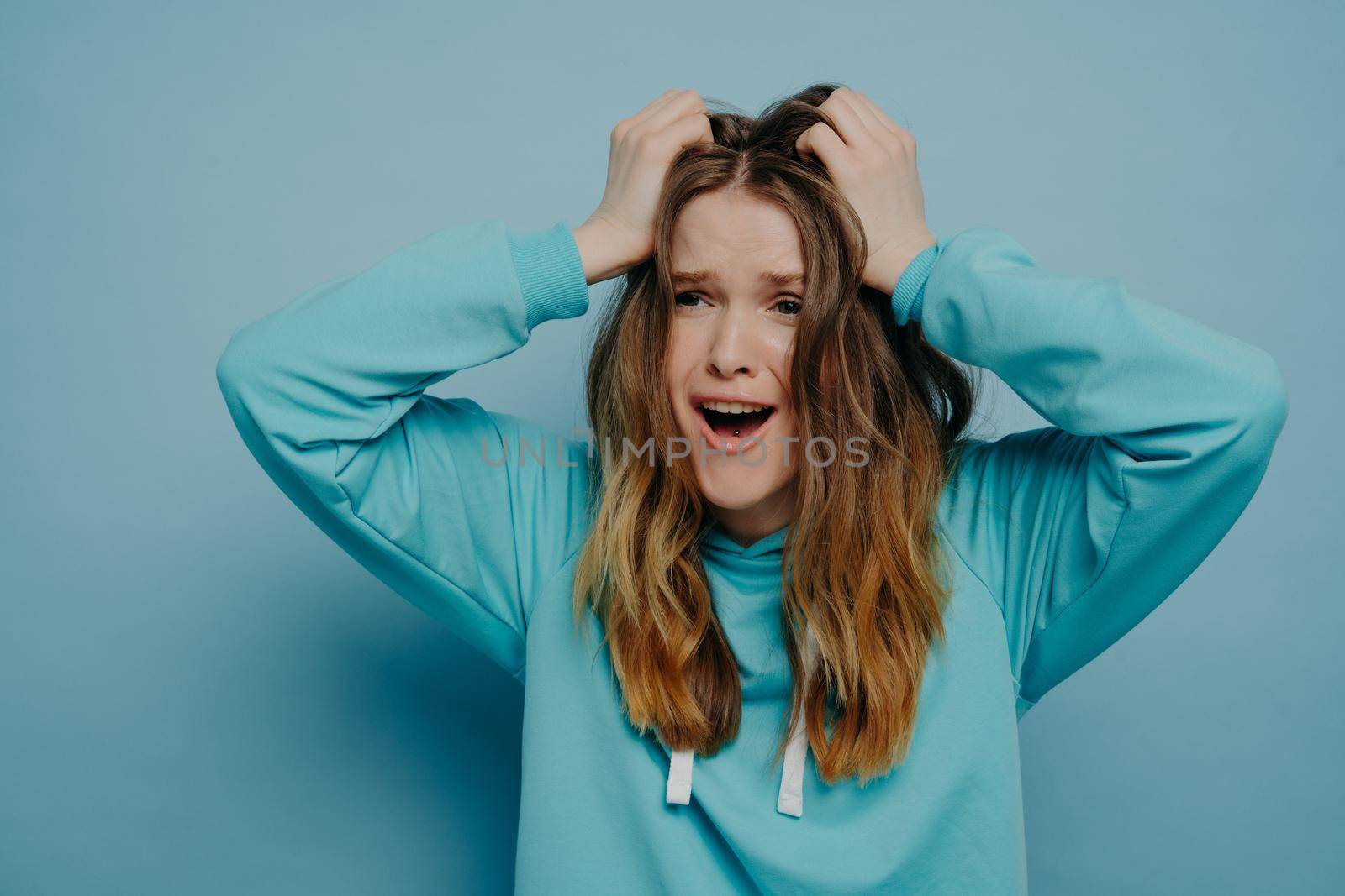 Pretty young female expressing shock and disbelief while holding head, screaming and looking away from camera with open mouth and eyebrows lowered. Negative human emotions concept