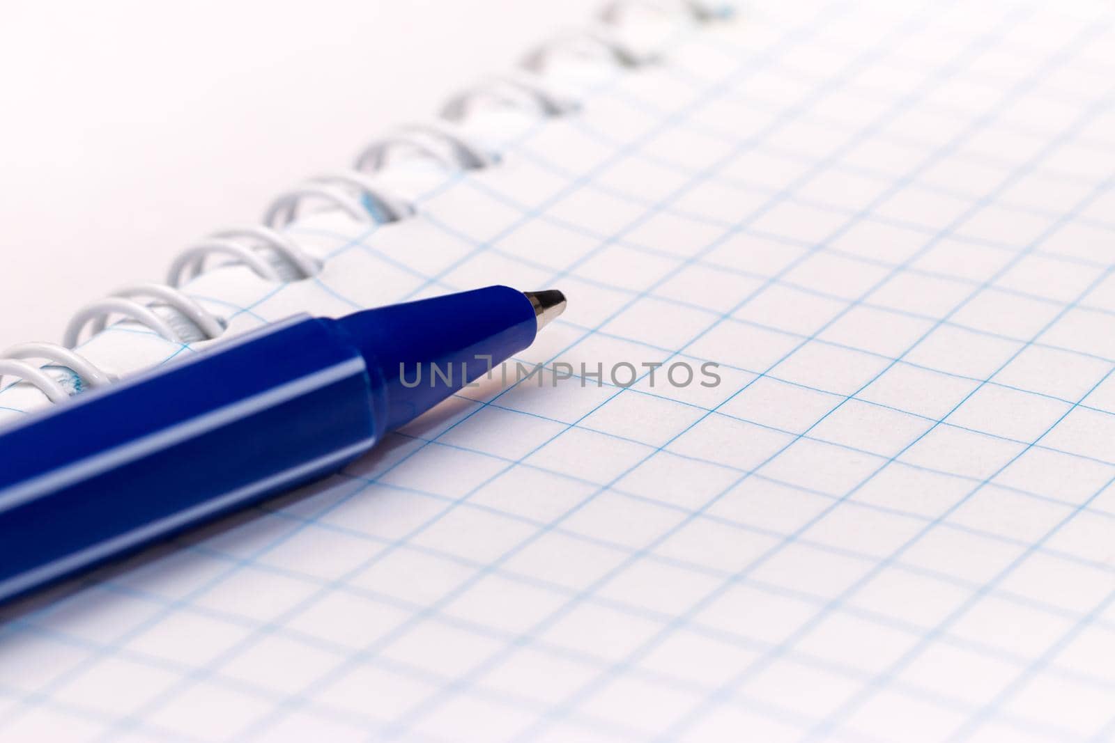 Blue ball pen on blank note book on white background. Close-up macro view