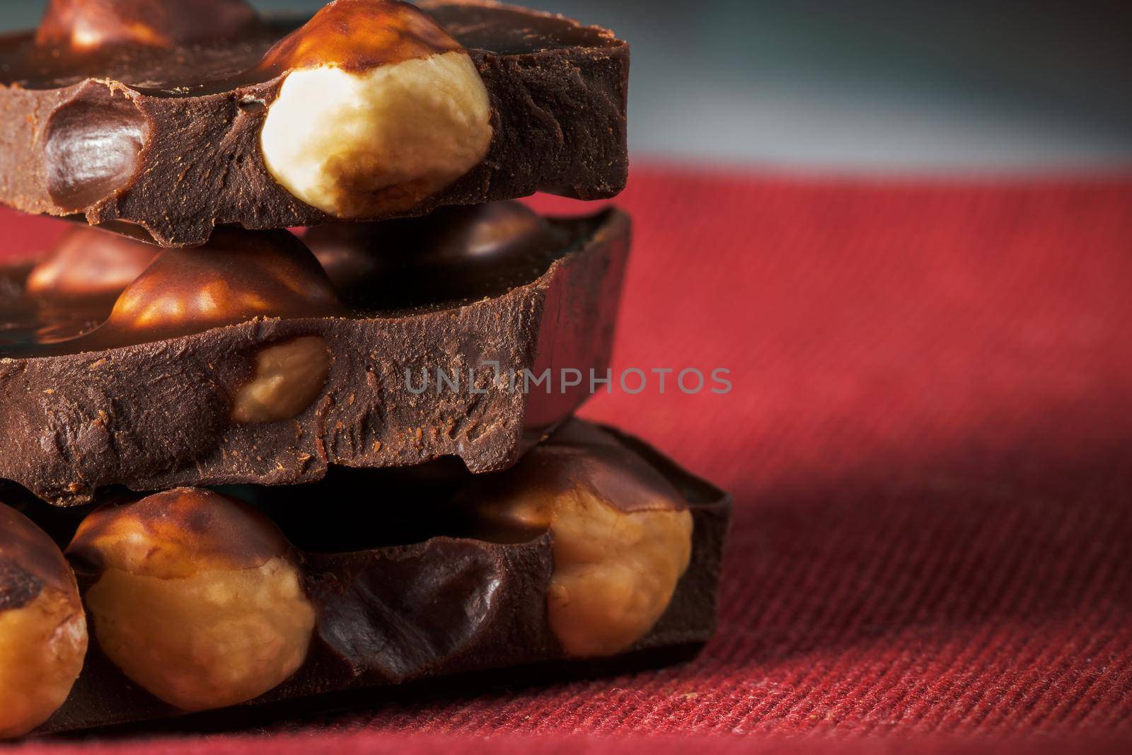 Slices of natural black chocolate with hazelnuts on a red napkin. Close-up macro view