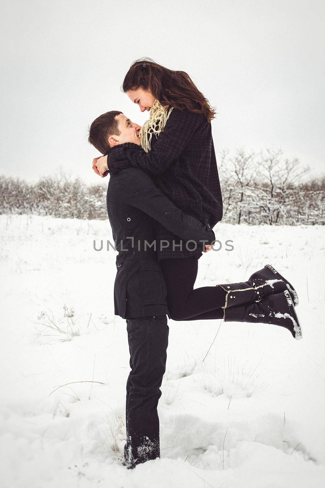 A guy and a girl in warm clothes and scarves on a walk in the snowy forest and in the field