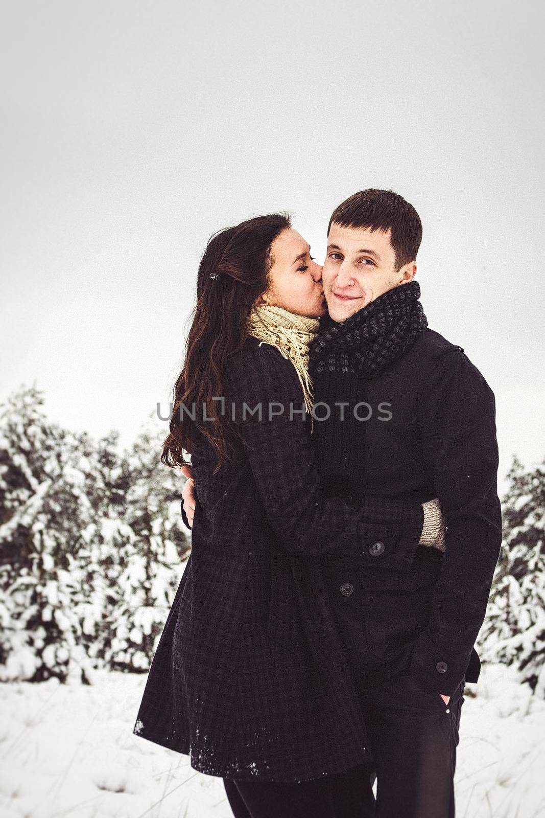 A guy and a girl in warm clothes and scarves on a walk in the snowy forest and in the field