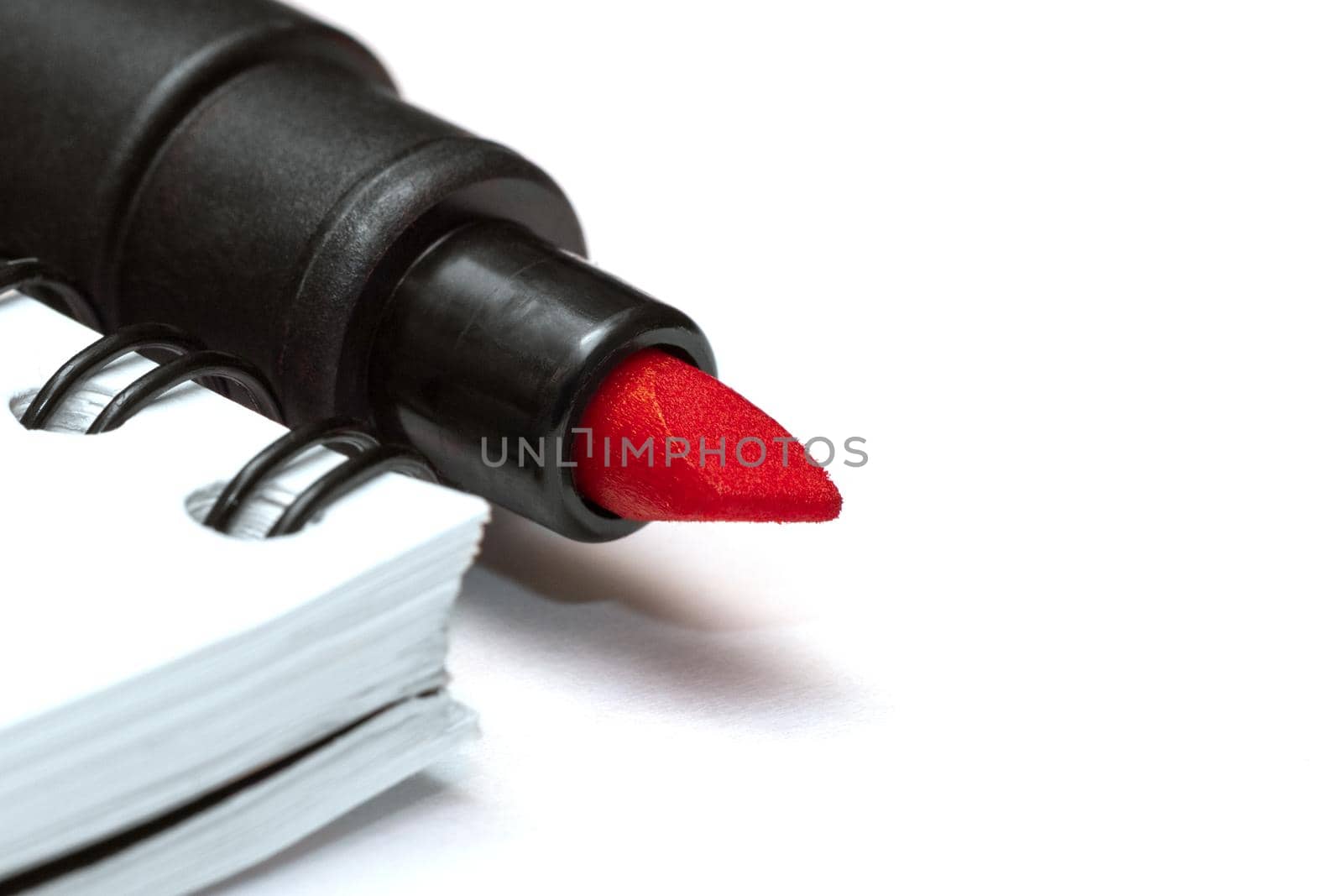 Red marker near a blank note book on white background. Close-up macro view