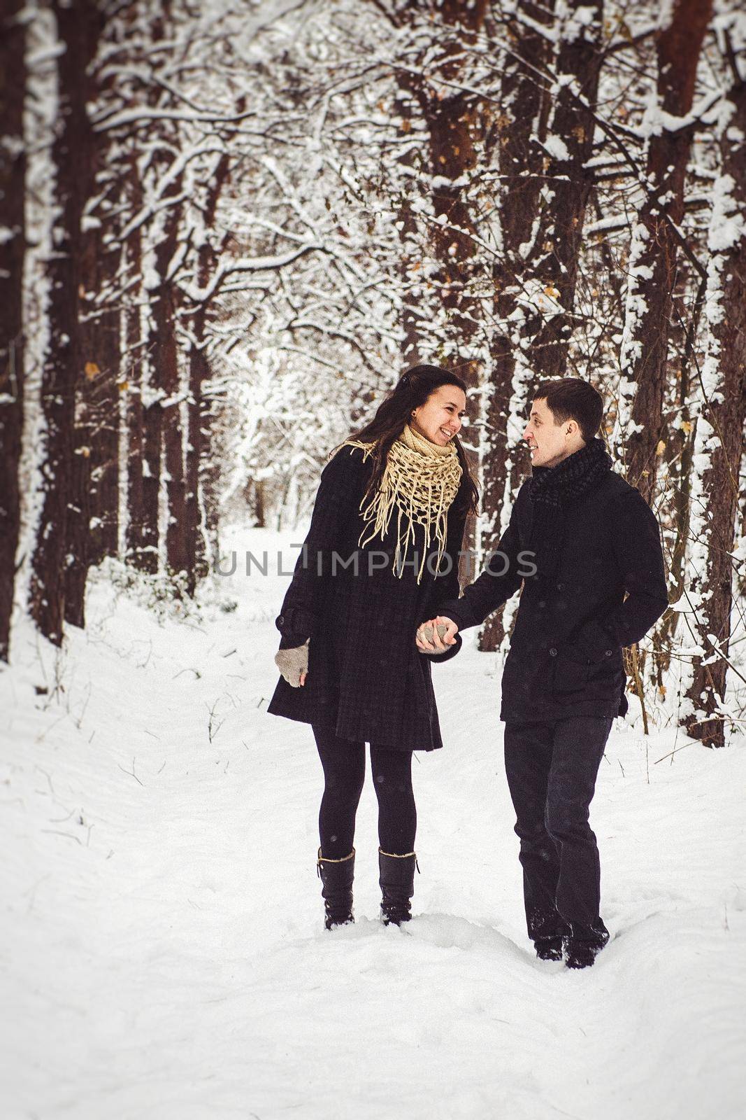 A guy and a girl in warm clothes and scarves on a walk in the snowy forest and in the field