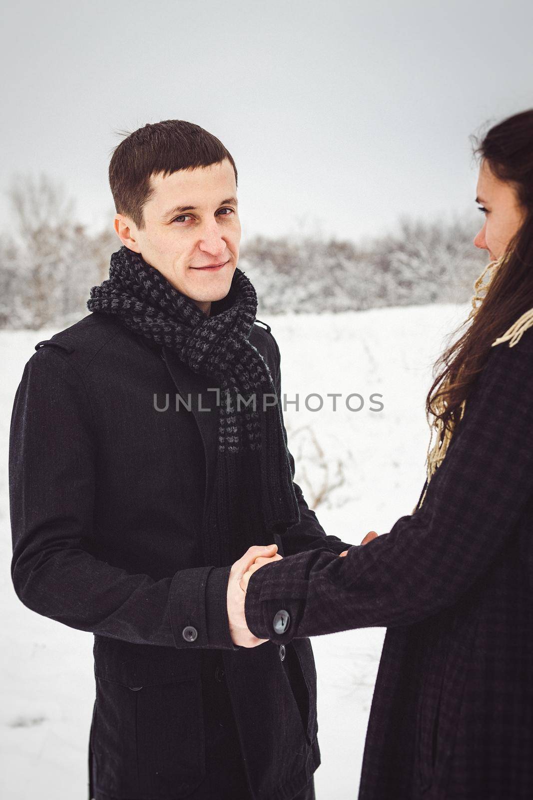 A guy and a girl in warm clothes and scarves on a walk in the snowy forest and in the field