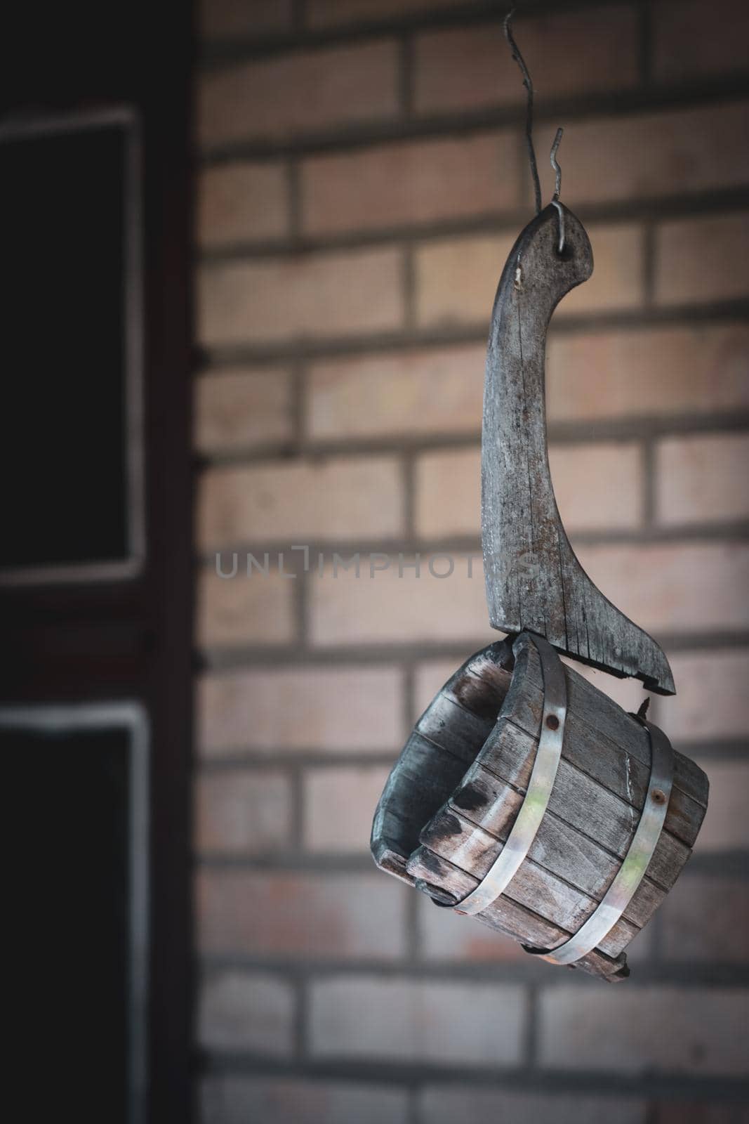 Old broken wooden ladle for russian bath hanging on a wire against a brick wall of the sauna. Vintage look