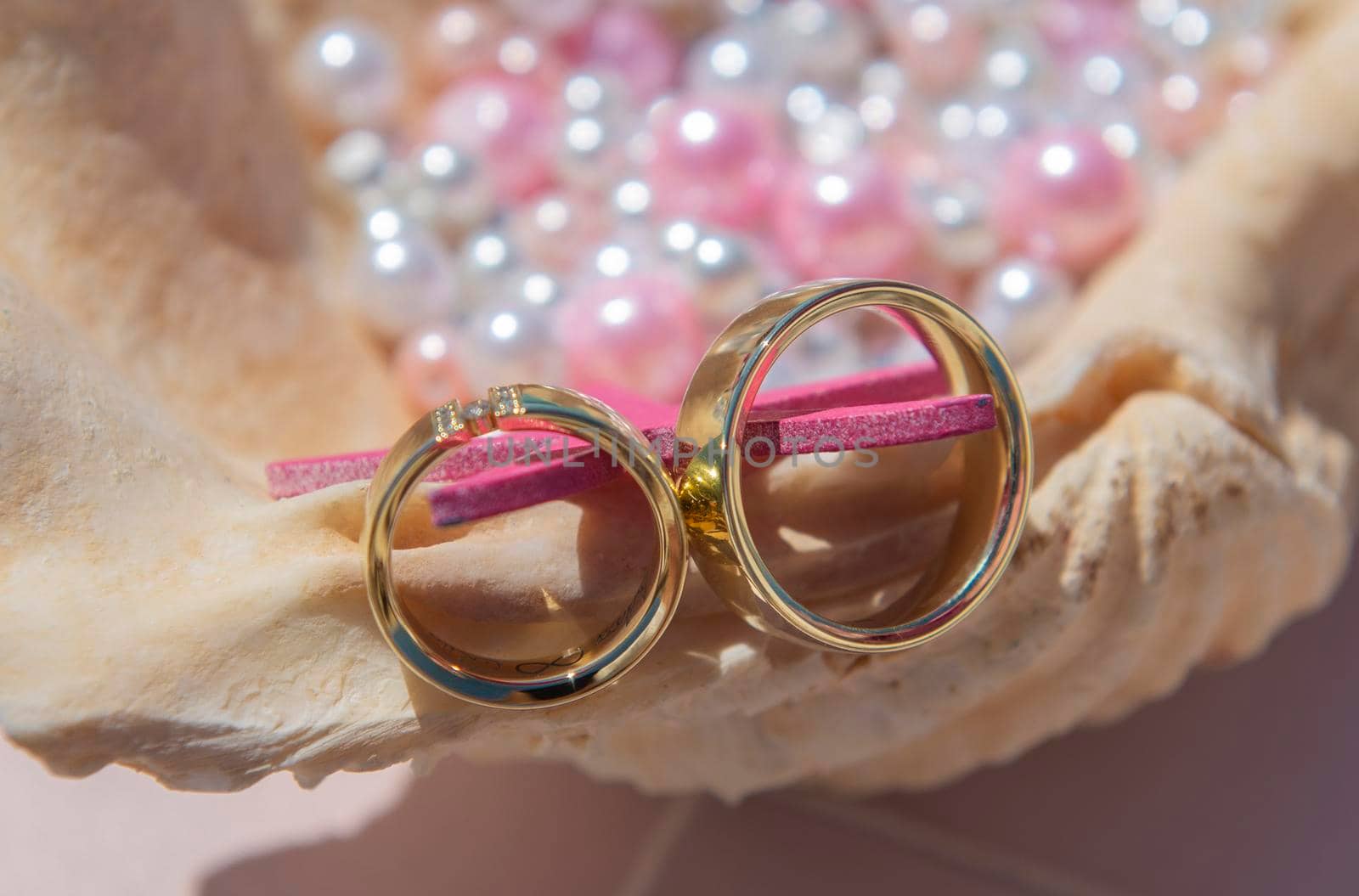 Pair of gold wedding ring bands jewelry on seashell with pink and white pearl beads