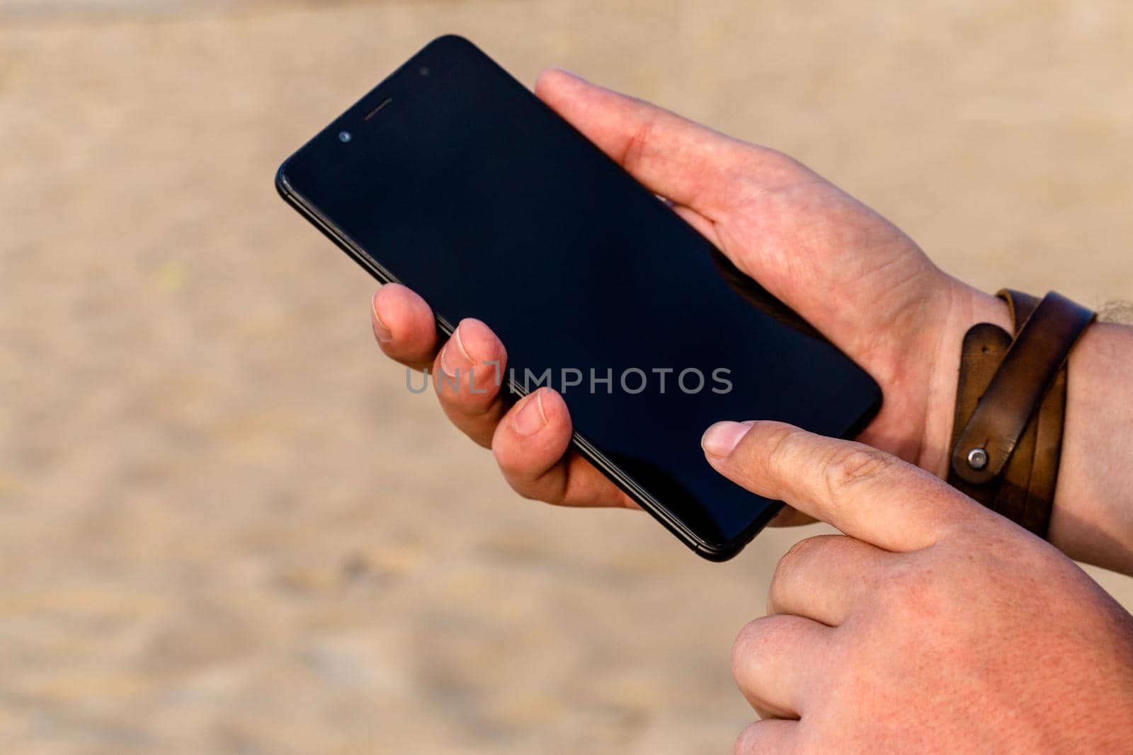 A man touching smartphone screen with his index finger on a beach sand background