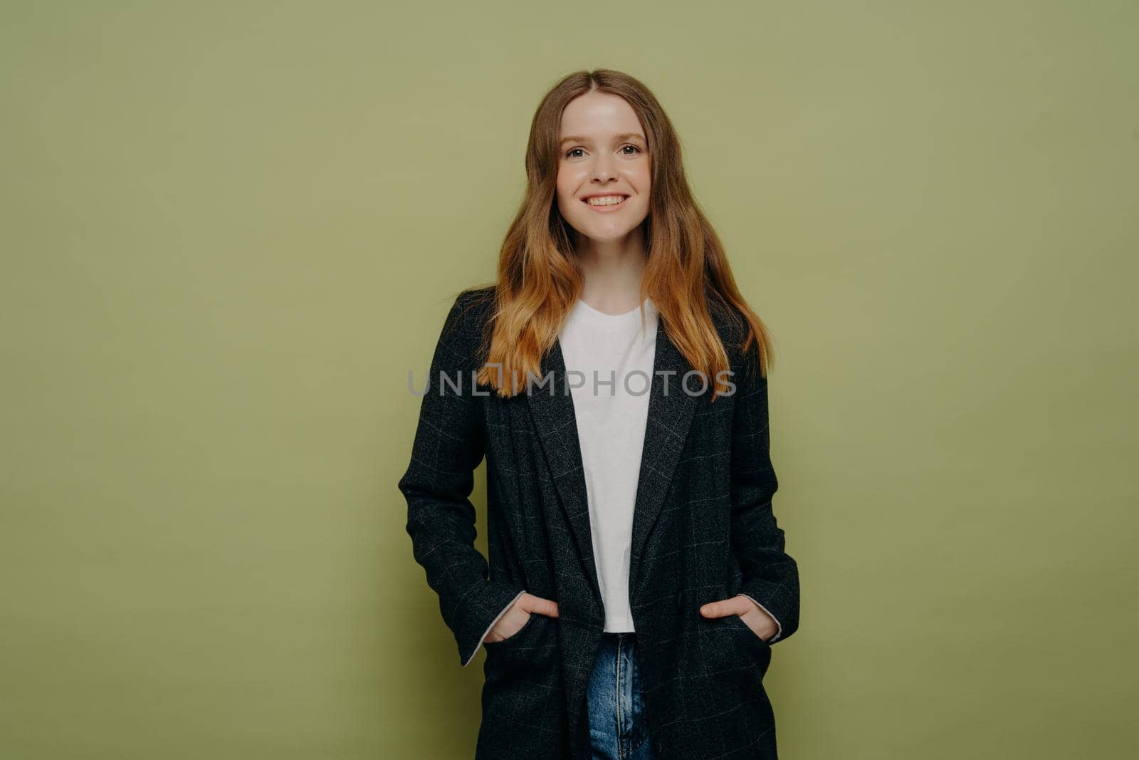Happy fashionable cheerful teenage girl wearing blazer and jeans with keeping hands in pockets and smiling at camera,young woman looking at camera with happy expression, studio shot