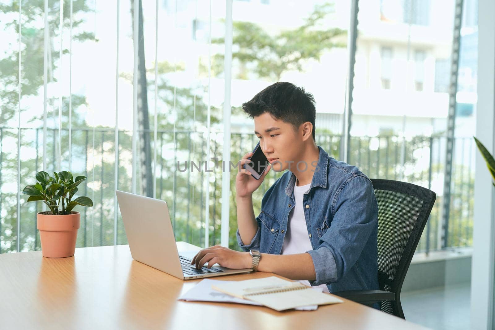  man talking on mobile phone, working from home. Portrait of pensive asian businessman using laptop computer, planning project, communication in modern office by makidotvn