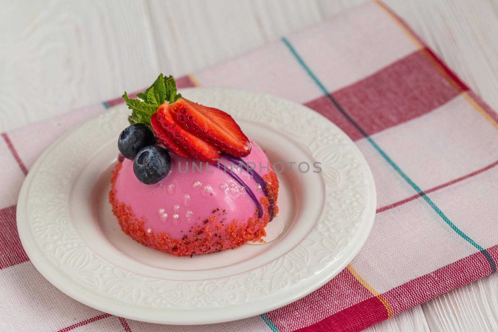 Blueberry mousse dessert on a dessert plate with confectionery glaze and sliced strawberries.