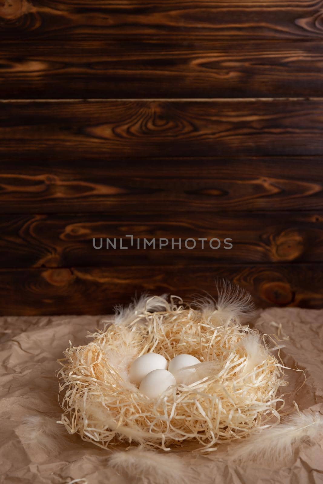 Chicken eggs lie on a wicked paper straw in a wicker basket on a dark wooden background in the morning sun