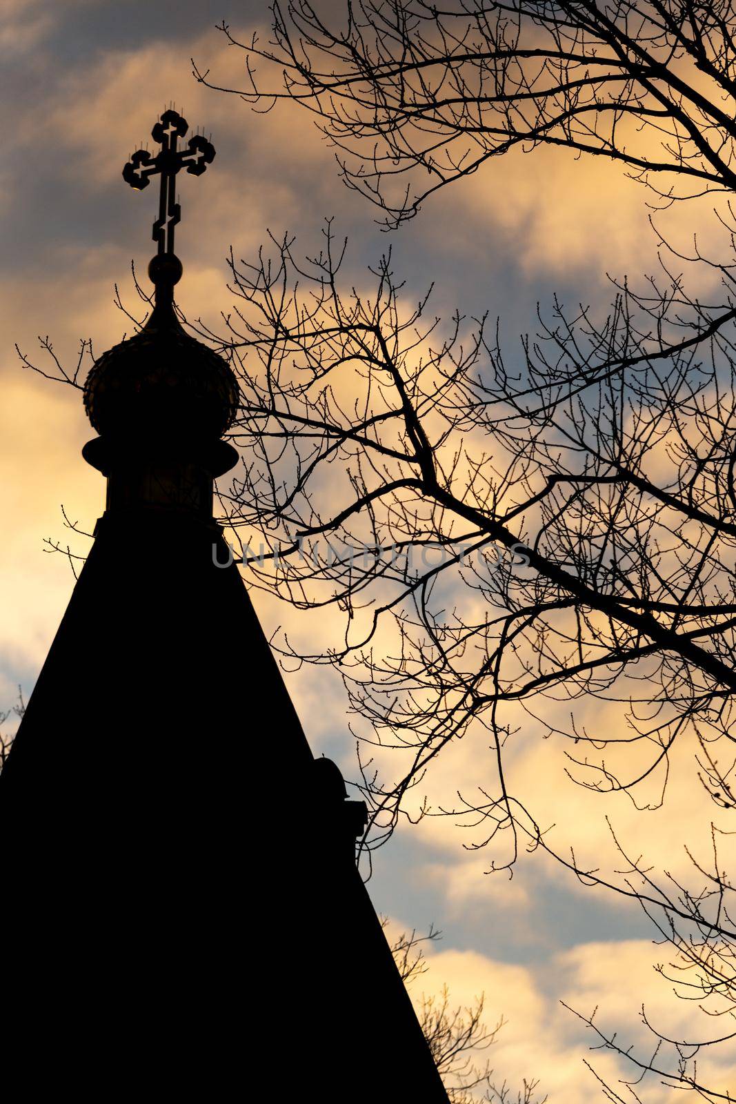Silhouette of the roof of the Orthodox Cathedral on a background of orange clouds on a blue sky