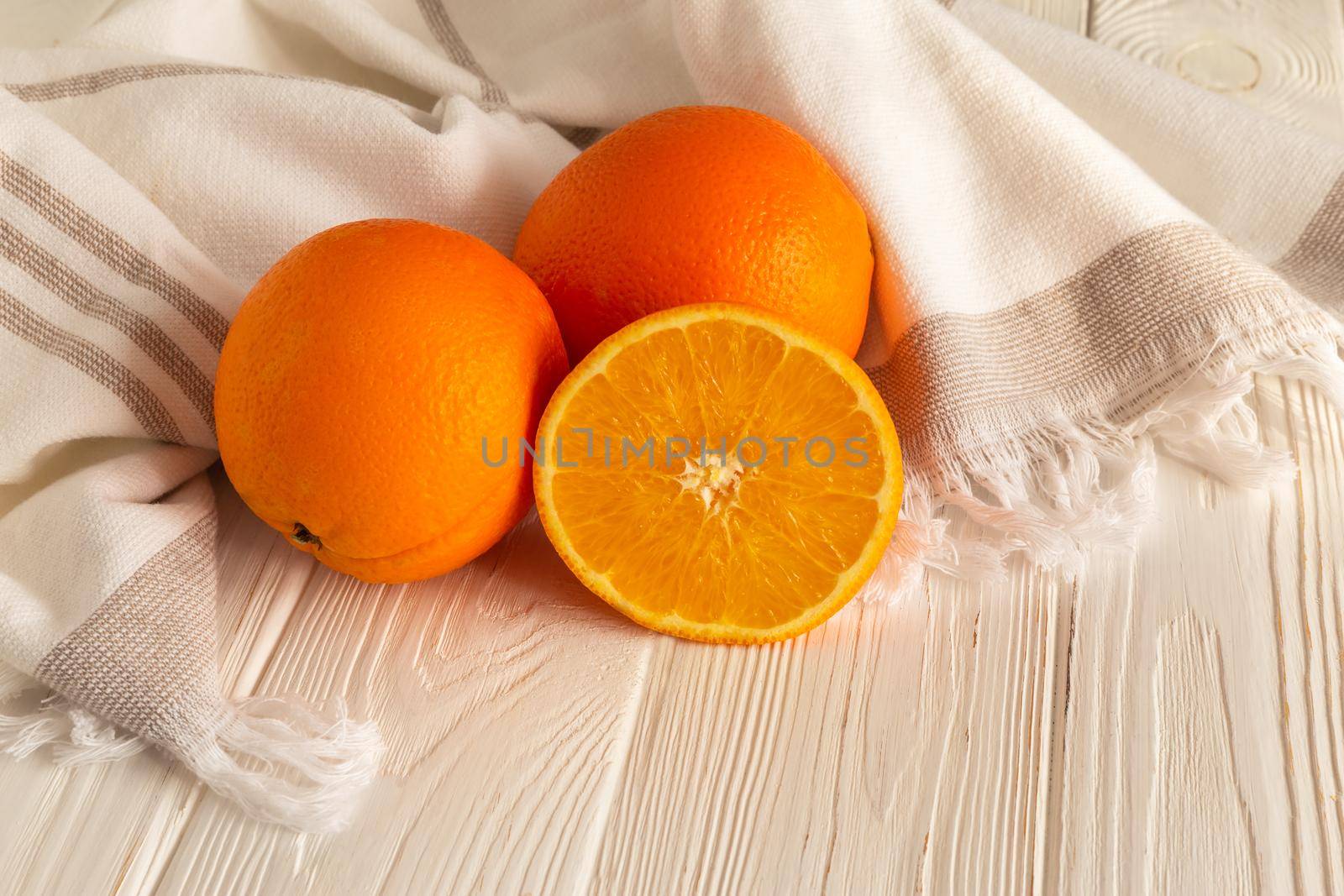 Orange on the white wooden kitchen table in linen towel under soft sunlight