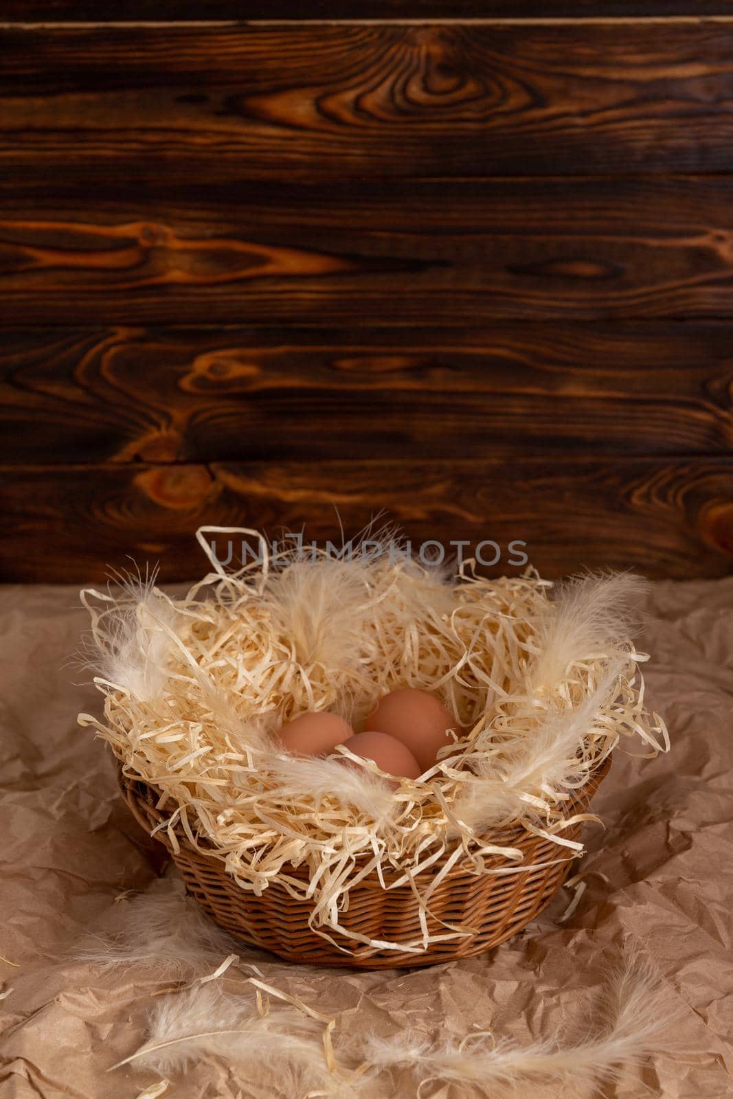 Chicken eggs lie on a wicked paper straw in a wicker basket on a dark wooden background in the morning sun