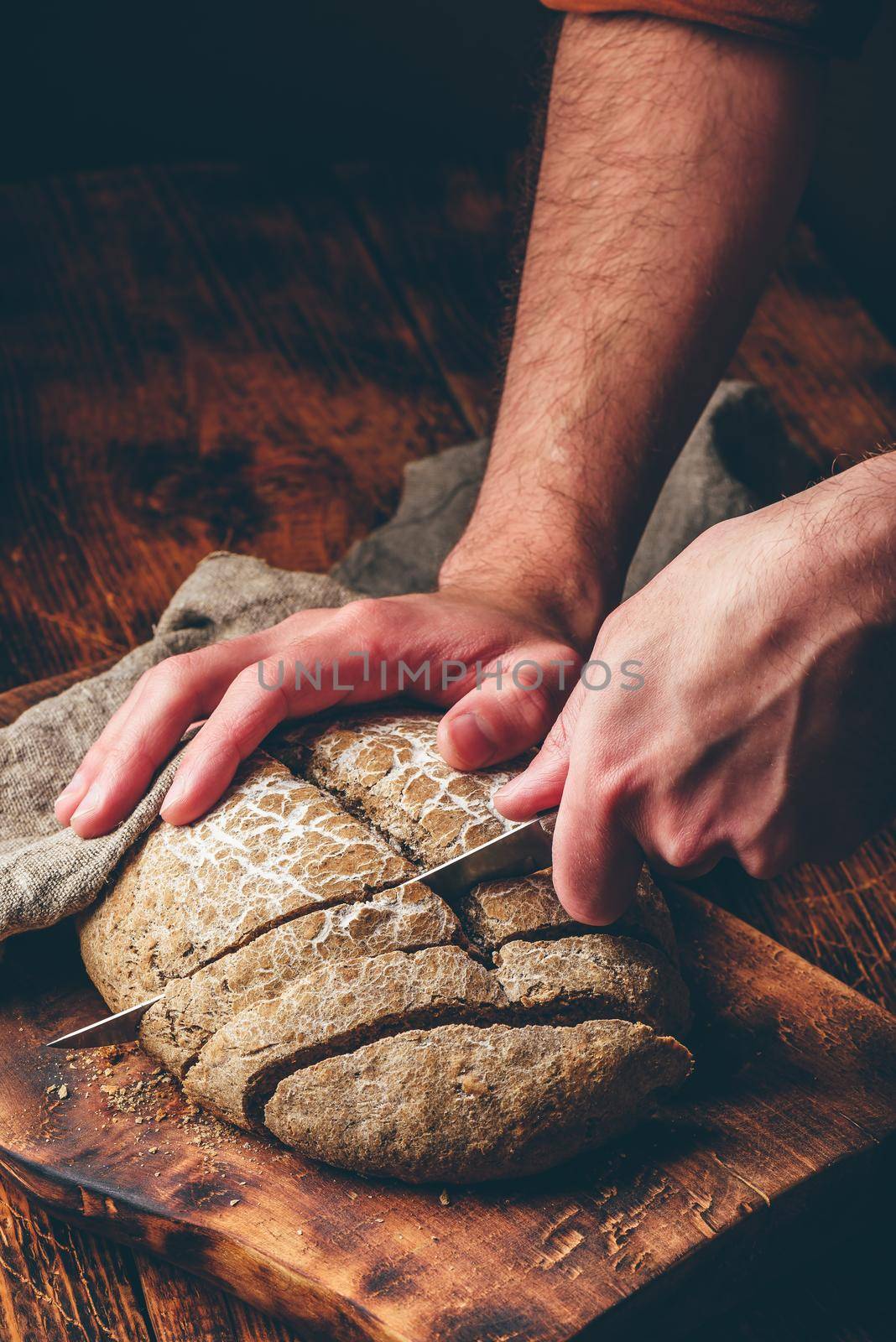 Baker slices loaf of homemade rye bread on cutting board