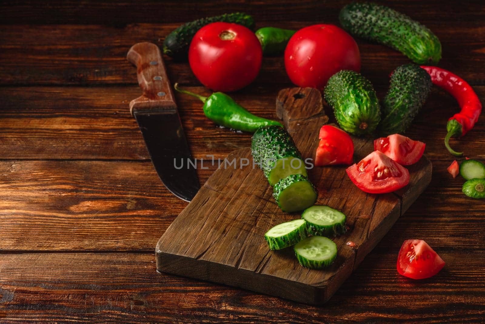 Sliced vegetables. Tomatoes, cucumbers and chili peppers over wooden background.