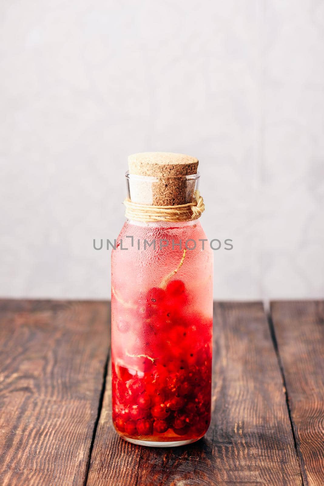 Red currant infused water with ice in glass bottle