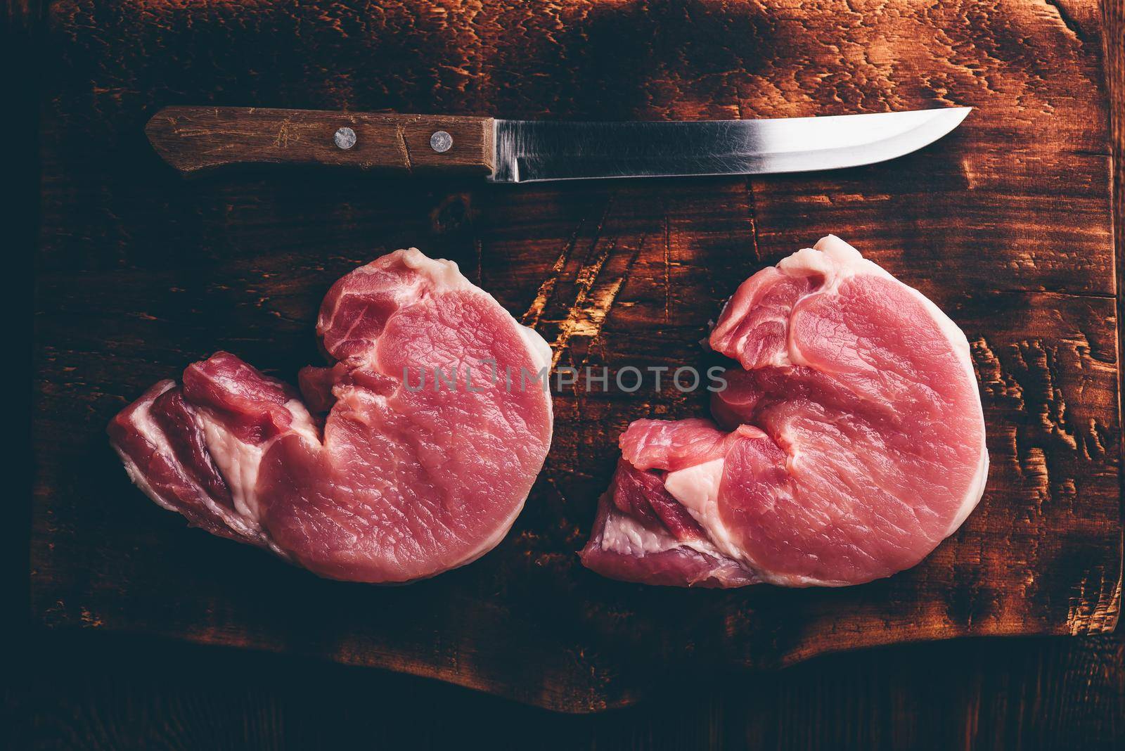 Two pork loin steaks with knife on rustic cutting board