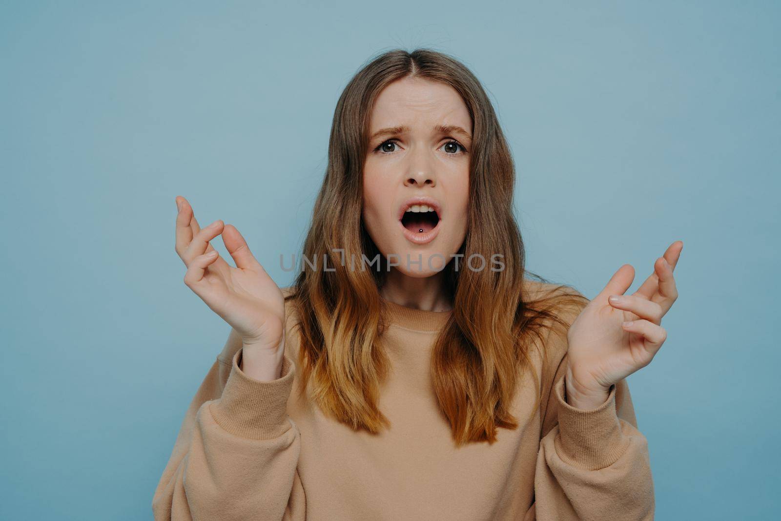 Cute teenage girl expressing disbelief and shock standing against blue studio wall by vkstock