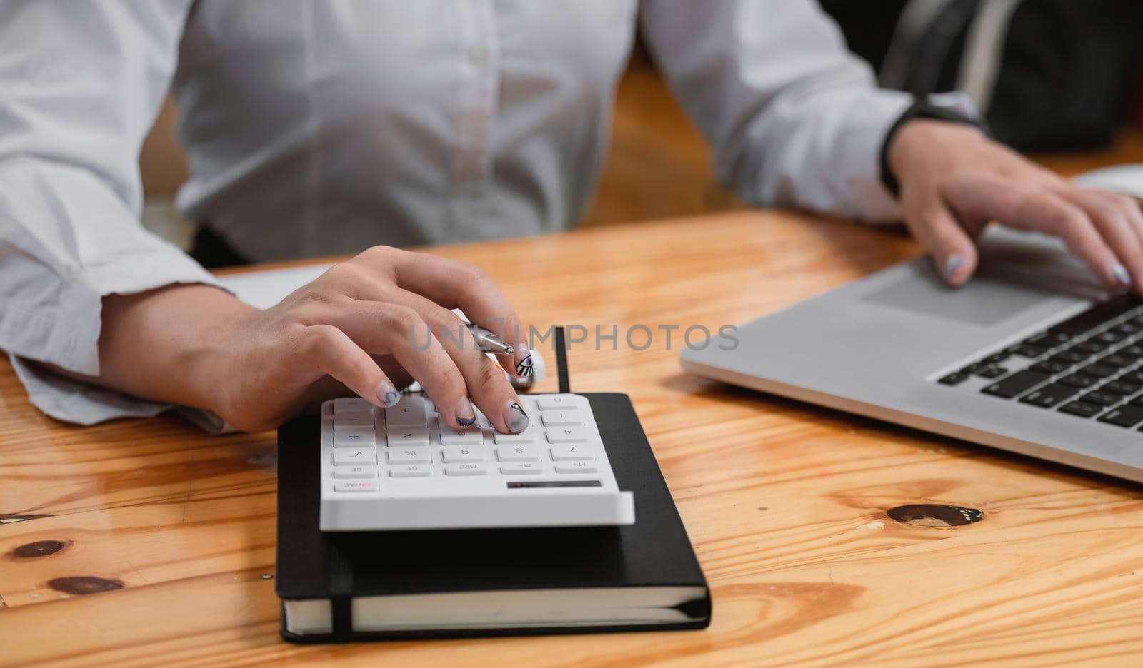 Businesswoman using calculator to calculate the numbers in the company financial report. Famale using laptop computer at her office.