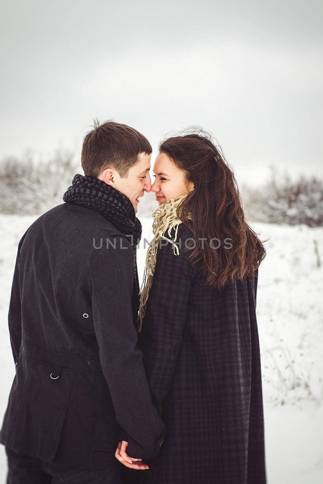 A guy and a girl in warm clothes and scarves on a walk in the snowy forest and in the field