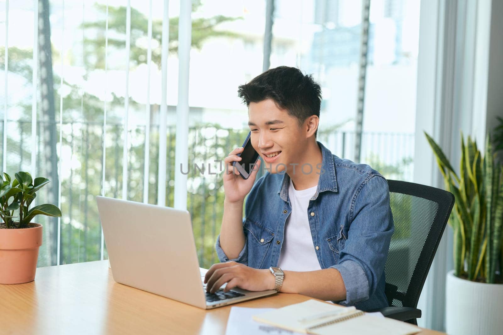  man talking on mobile phone, working from home. Portrait of pensive asian businessman using laptop computer, planning project, communication in modern office