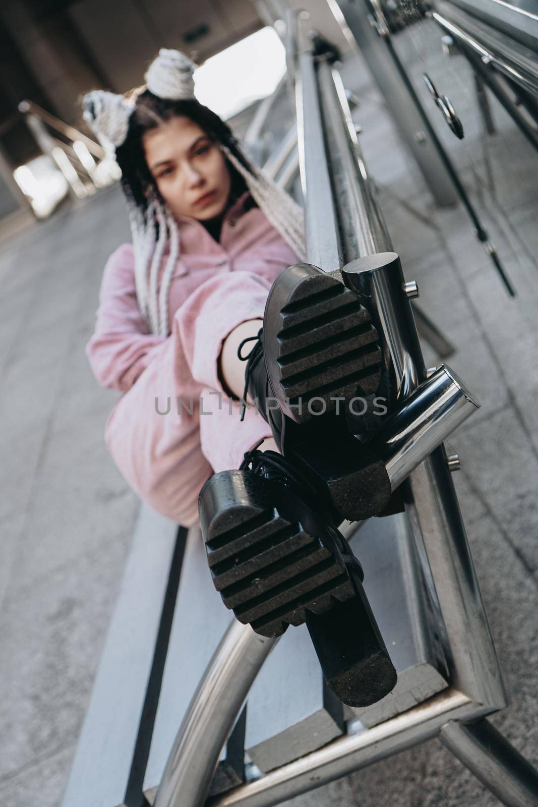 Young woman with futuristic looks. Girl with black and white dreadlocks or pigtails. Against the background of a futuristic building. Focus on shoes