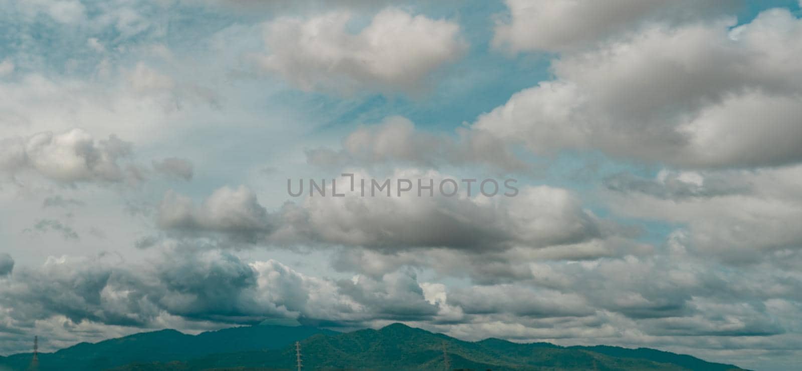 Panorama view of the overcast sky above the green mountain and electric pylons. Dramatic sky and cumulus clouds. Cloudy and moody sky. Storm sky. Cloudscape. Overcast clouds. Beauty in nature.