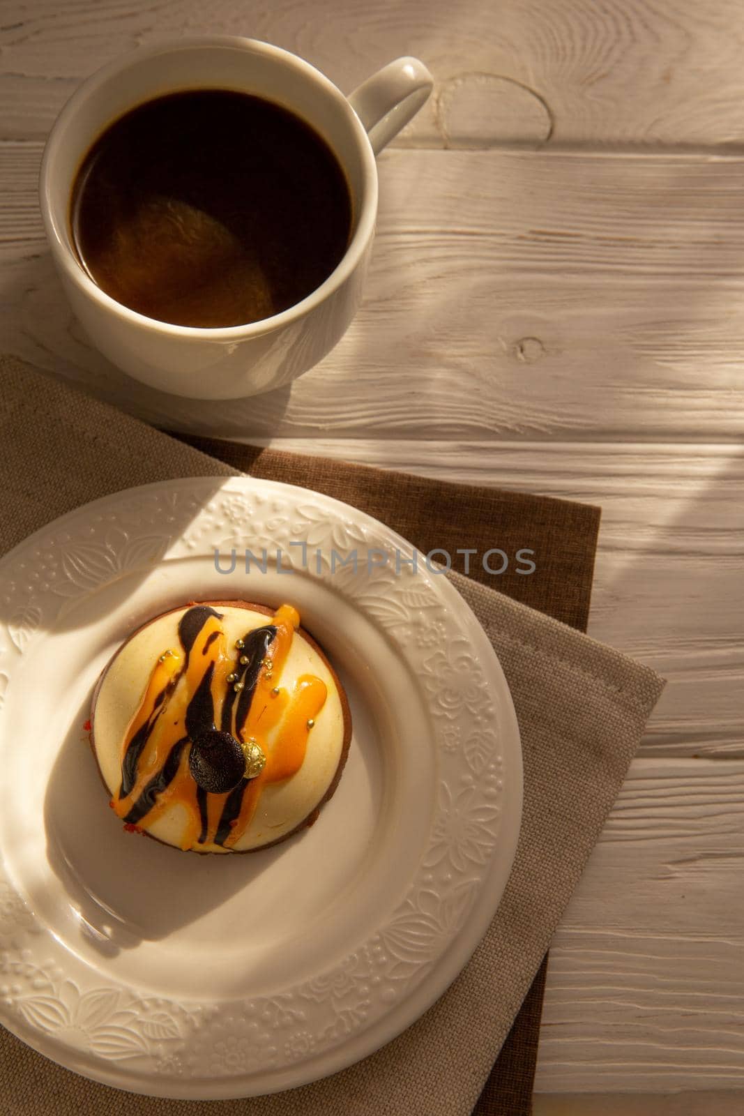 Still life with a cup of coffee and sweet cake on white wooden table. Breakfast in the morning sun