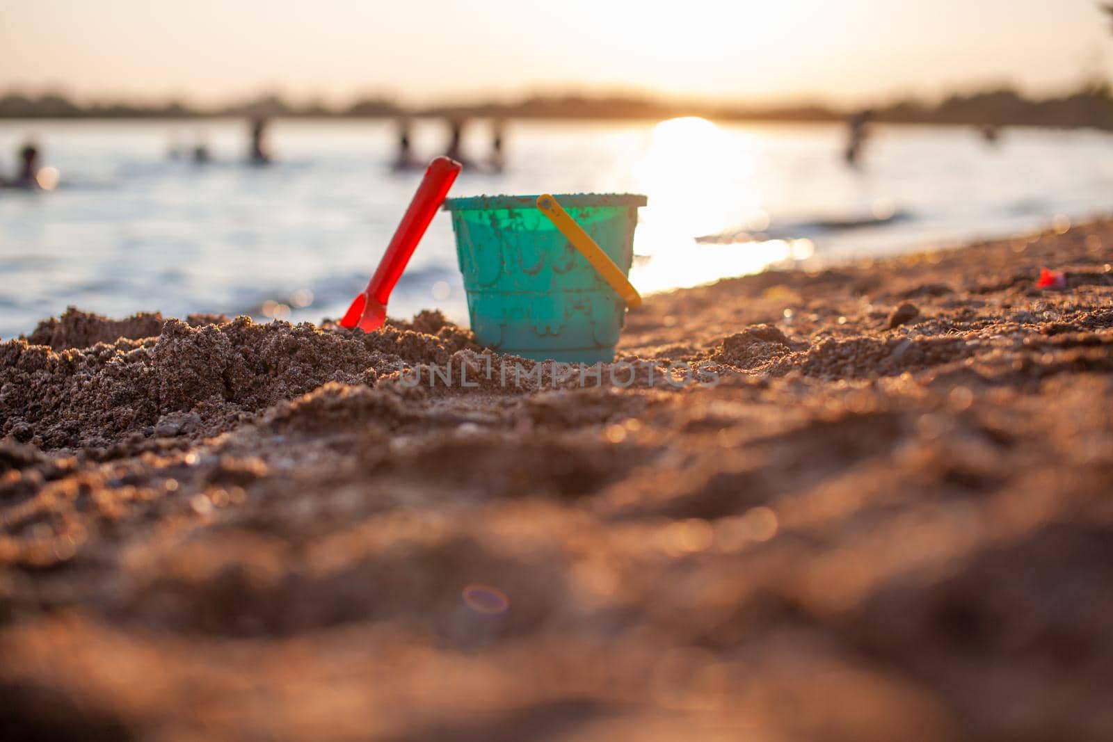 Children's toys for playing on the sand. Plastic bucket and rake on the beach at sunset. The concept of summer, family holidays and vacations.